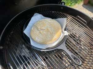 Half-baked loaf of sourdough on a cast iron skillet atop a grill