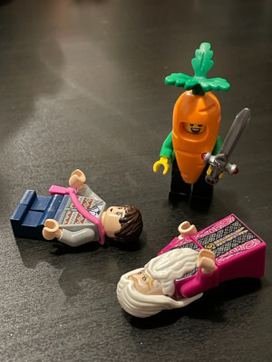 A Lego minifigure wearing a carrot outfit and wielding a sword stands above two fallen Lego minifigures