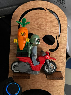 Two Lego minifigures on a Lego motorbike. Facing forward (relative to the bike) is Boba Fett. Facing to the side (and facing the camera) is a minifigure wearing a carrot outfit