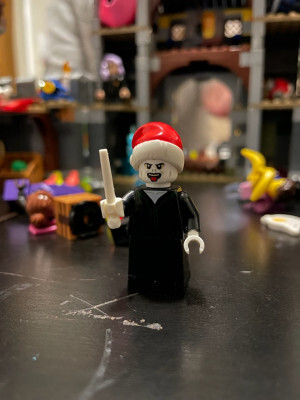 Lego Voldemort minifigure wearing a Santa hat standing before a blurry background of Lego chaos