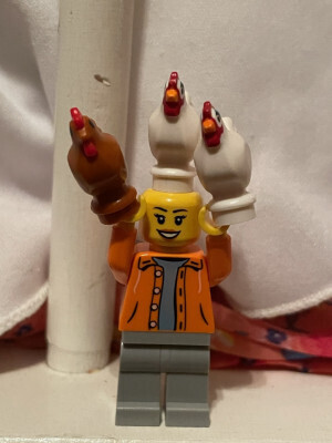 Lego minifigure with three Lego chickens - one on her head and one in each hand