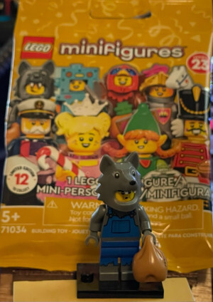 Lego wolf minifigure in front of the bag it came in. Bag says series 23 and includes among various figures a Lego figure in a chicken suit