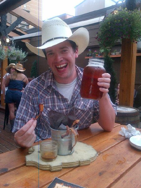 Pete in a cowboy hat holding a beer and eating bacon from a bucket