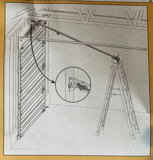 An image from garage door opener installation instructions, showing a closed garage door and a ladder near it. The rail for the garage door opener is attached above the garage door and the garage door opener is not yet mounted but instead sits atop the ladder