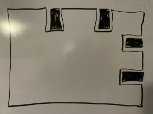 A dry erase board drawing of a top view of the shelf. It is a rectangle, but the top and right sides each have two cut outs to accommodate studs