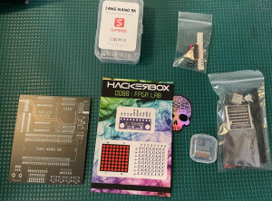 Components of HackerBox 0088 - an unpopulated PCB for an FPGA lab, an FPGA board, a sticker, other misc electronic components